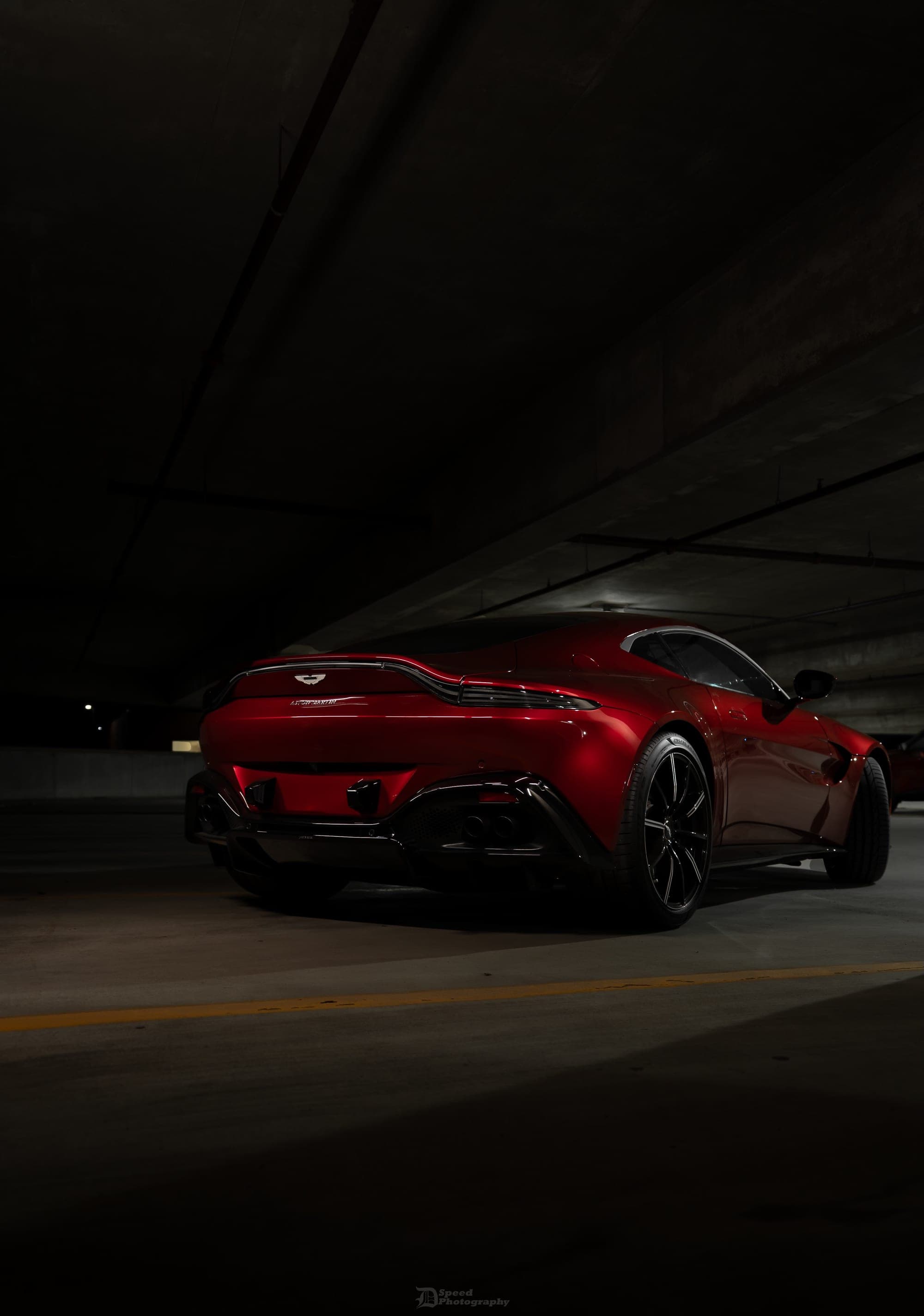 Red Aston Martin Vantage parked in a parking garage, rear three-quarter view